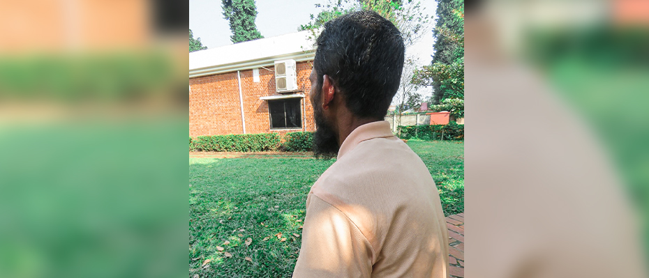 Rahman sits outside in a garden and faces away from the camera to protect his identity